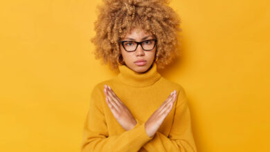 blond-curly-haired-woman-shows-cross-makes-stop-gesture-says-no-with-angry-expression-declines-something-wears-spectacles-long-sleeved-jumper-isolated-yellow-background-its-taboo