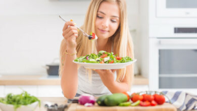 jeune-fille-blonde-heureuse-mangeant-salade-santé-d'araucula-d'épinards-de-tomates-d'olives-d'oignons-d'huile-d'olives