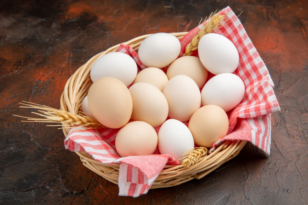 vue-devant-oeufs-de-poule-blancs-au-côté-du-panier-avec-serviette-surface-foncée