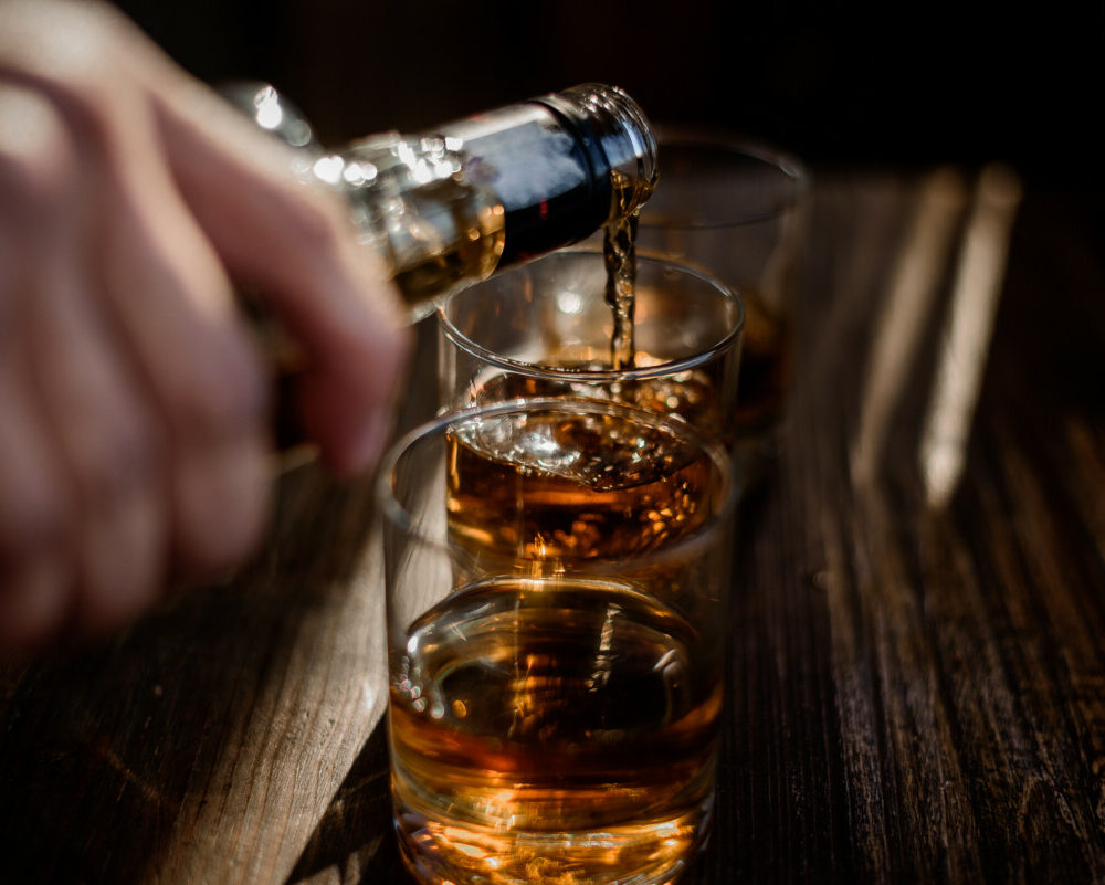 pouring-strong-alcohol-drink-into-glasses-which-are-wooden-table