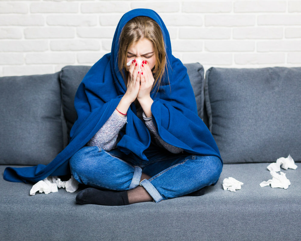 sick-woman-with-rheum-headache-holding-napkin-sitting-sofa-with-coverlet-pills-home