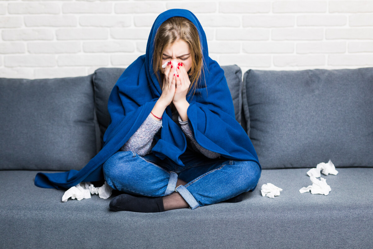 sick-woman-with-rheum-headache-holding-napkin-sitting-sofa-with-coverlet-pills-home