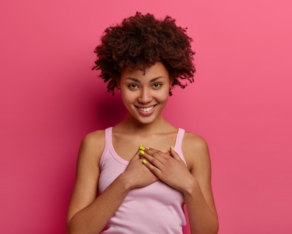 touched-pleased-lovely-woman-hears-heartwarming-story-presses-hands-heart-feels-thankful-promises-you-smiles-gently-wears-casual-clothes-appreciates-nice-gift-poses-rosy-wall