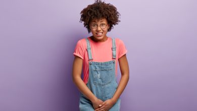 unhappy-dark-skinned-woman-holds-crotch-needs-toilet-has-problematic-situation-wears-pink-t-shirt-denim-sarafan-suffers-from-cystitis-isolated-purple-wall-people-urgency